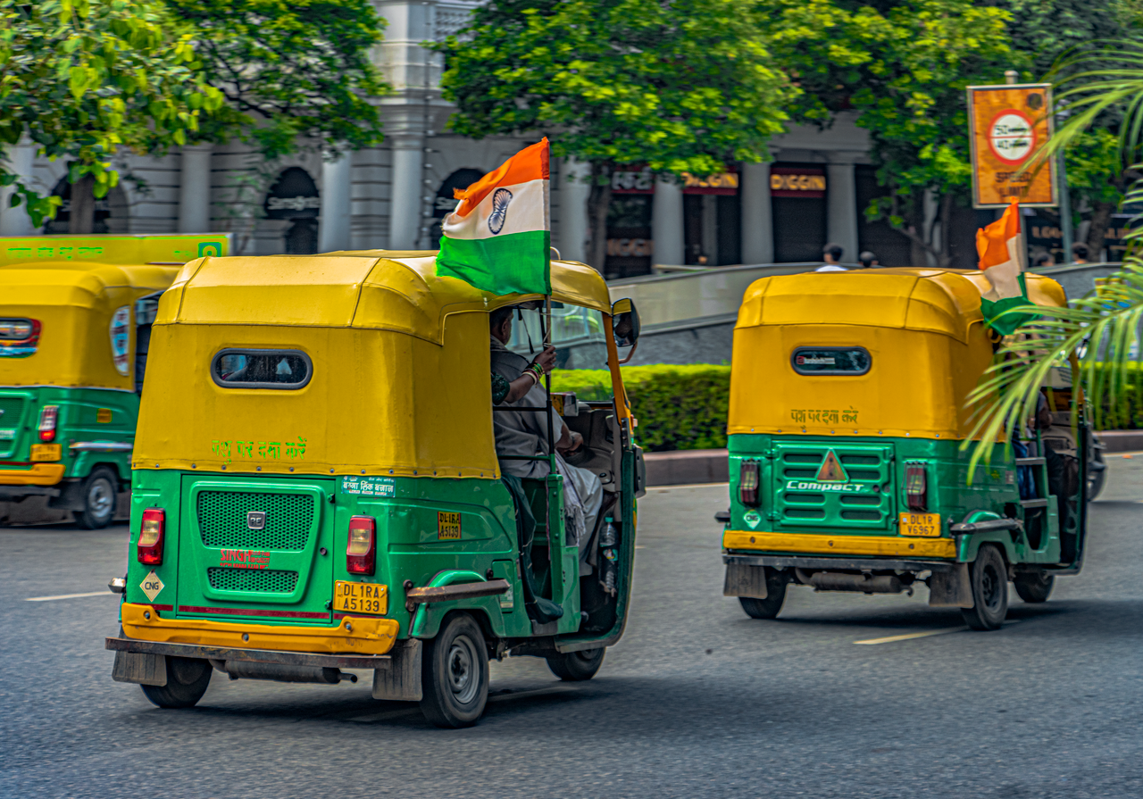 Auto rickshaws adorned with Indian flags driving through Connaught Place in New Delhi, India.